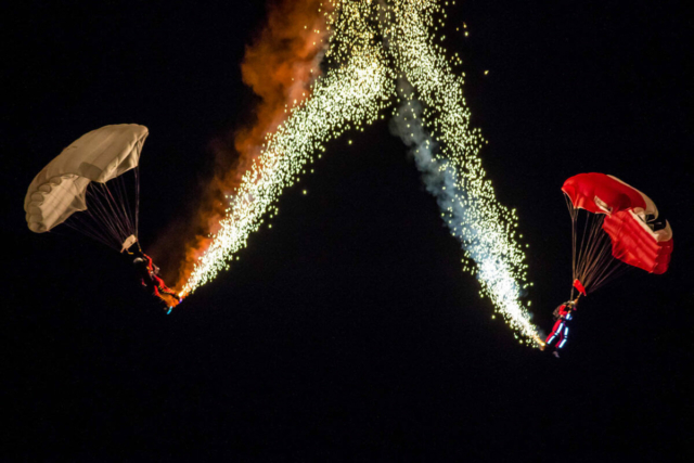 Two parachutists dropping in the night sky with pyrotechnics coming of them