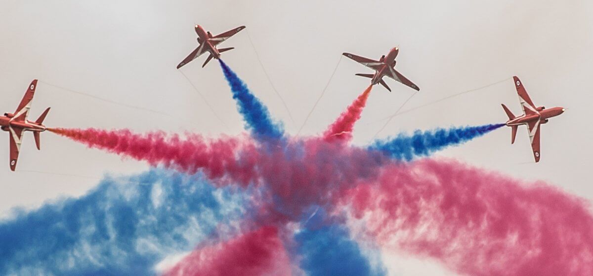 Red arrows fly in formation with blue and red smoke coming out of them