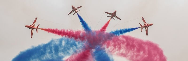 Red arrows fly in formation with blue and red smoke coming out of them