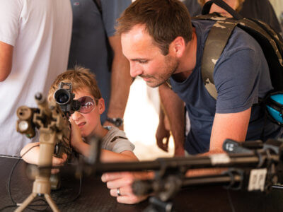 Kid looking through gun scope with his father next to him