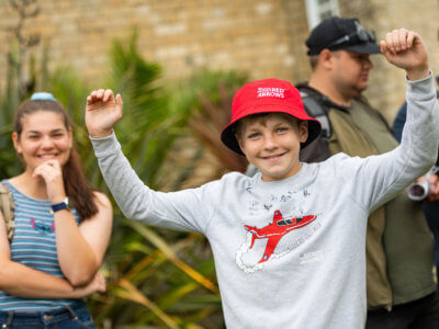 Kid in red arrows hat with hands in the air smiling for the camera